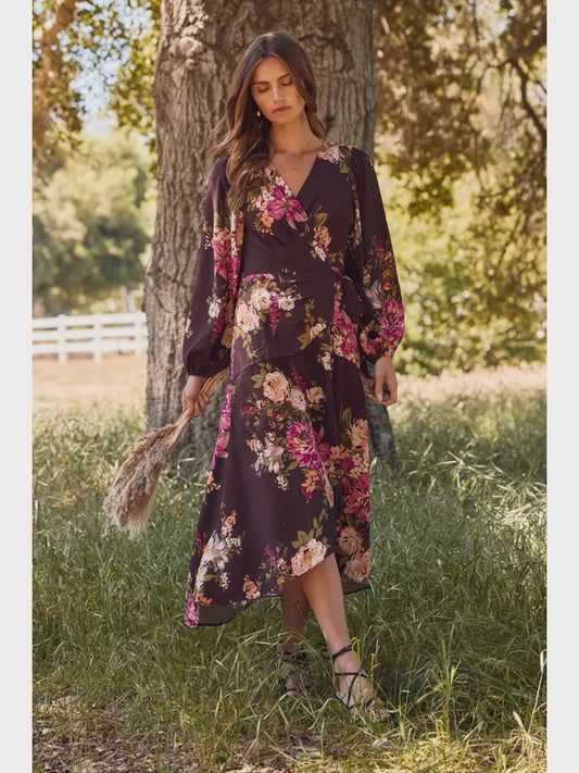 Woman in a floral dress standing in a grassy field with trees in the background