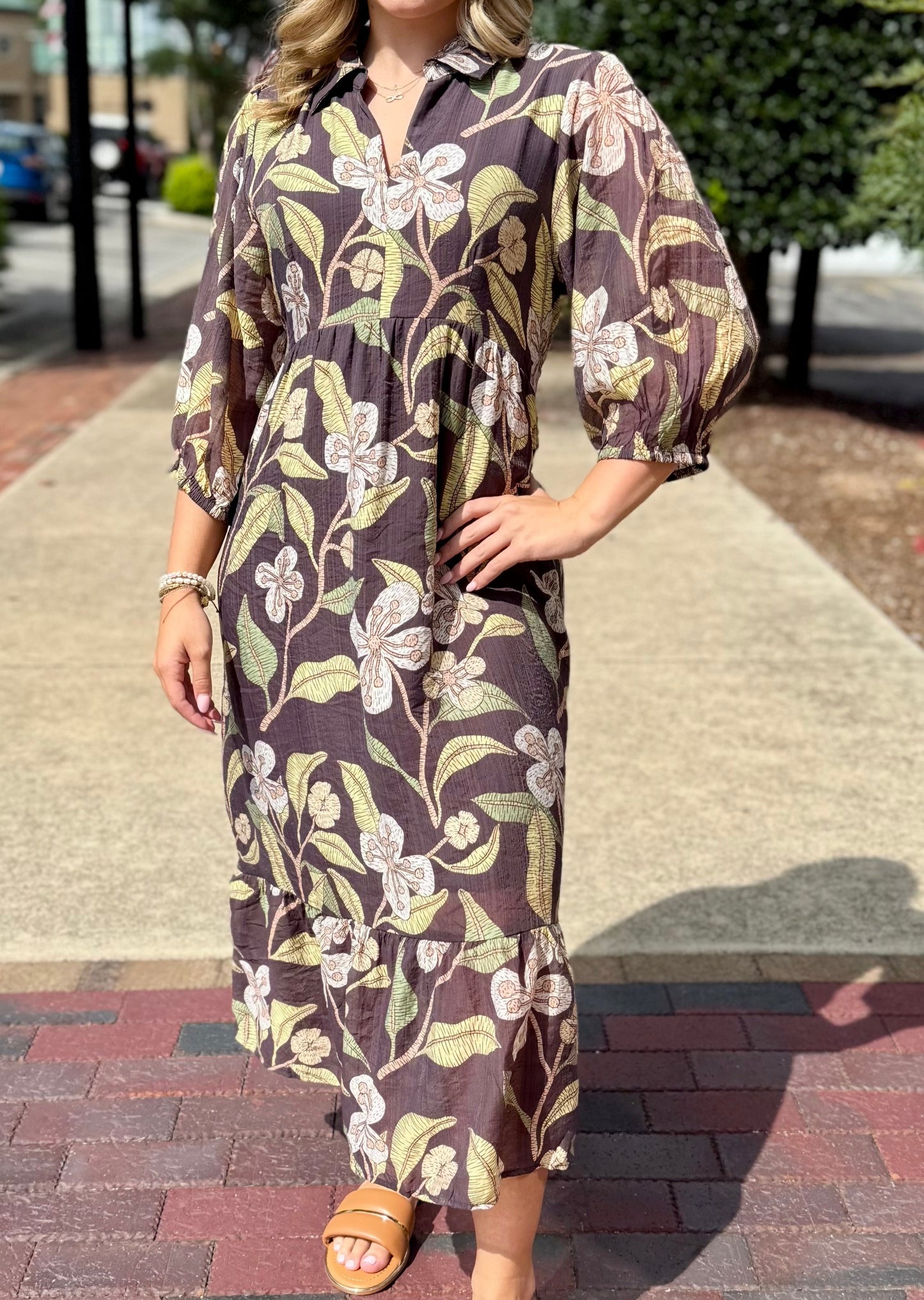 Woman wearing a floral dress on a sidewalk with trees and buildings in the background