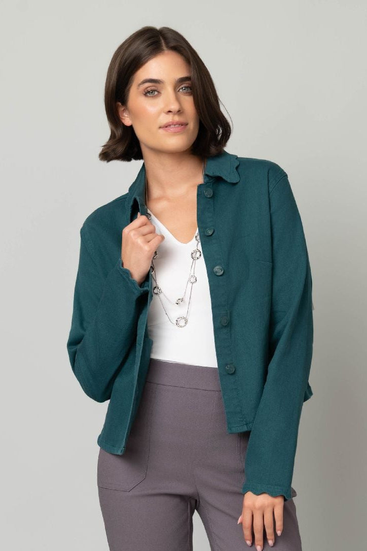 Woman wearing a teal jacket, white shirt, gray pants, and white shoes on a light gray background