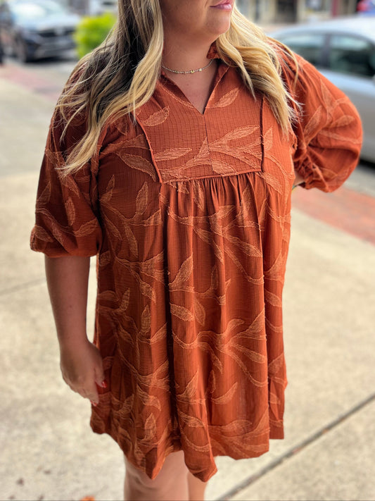 Woman wearing a rust-colored dress with leaf pattern on a city street.