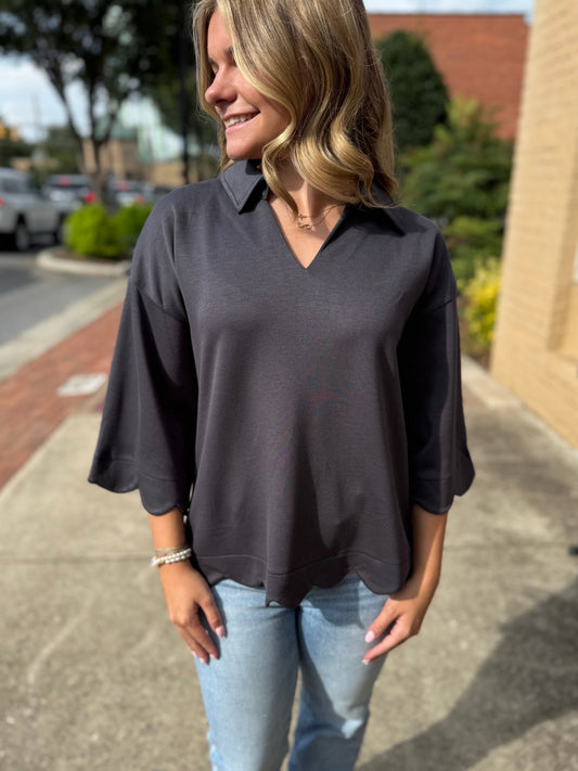 Woman wearing a dark gray shirt and light blue jeans standing on a sidewalk.