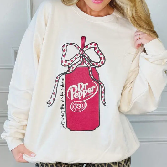 Woman wearing a cream sweatshirt with a Dr Pepper logo and leopard print pants against a white wall.
